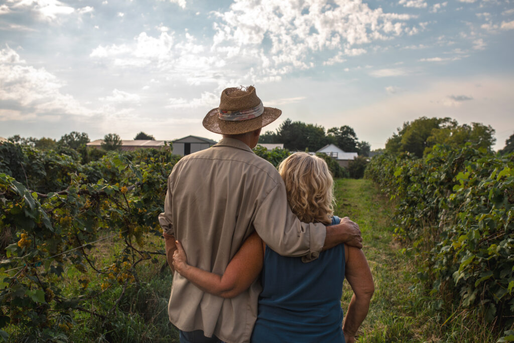 Couple standing in field looking down path toward farmhouse