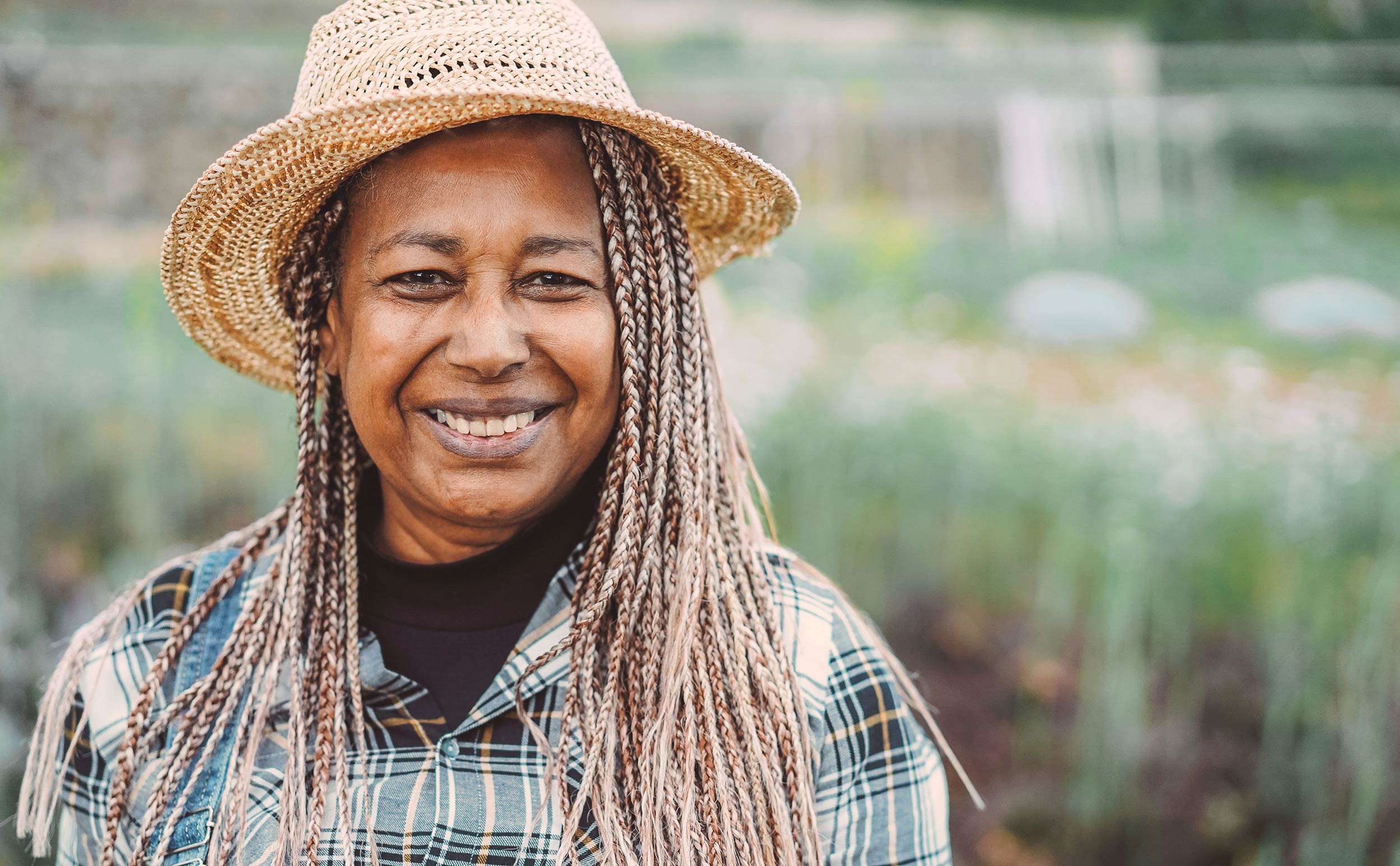 Smiling woman outdoors wearing a hat and braided hair.