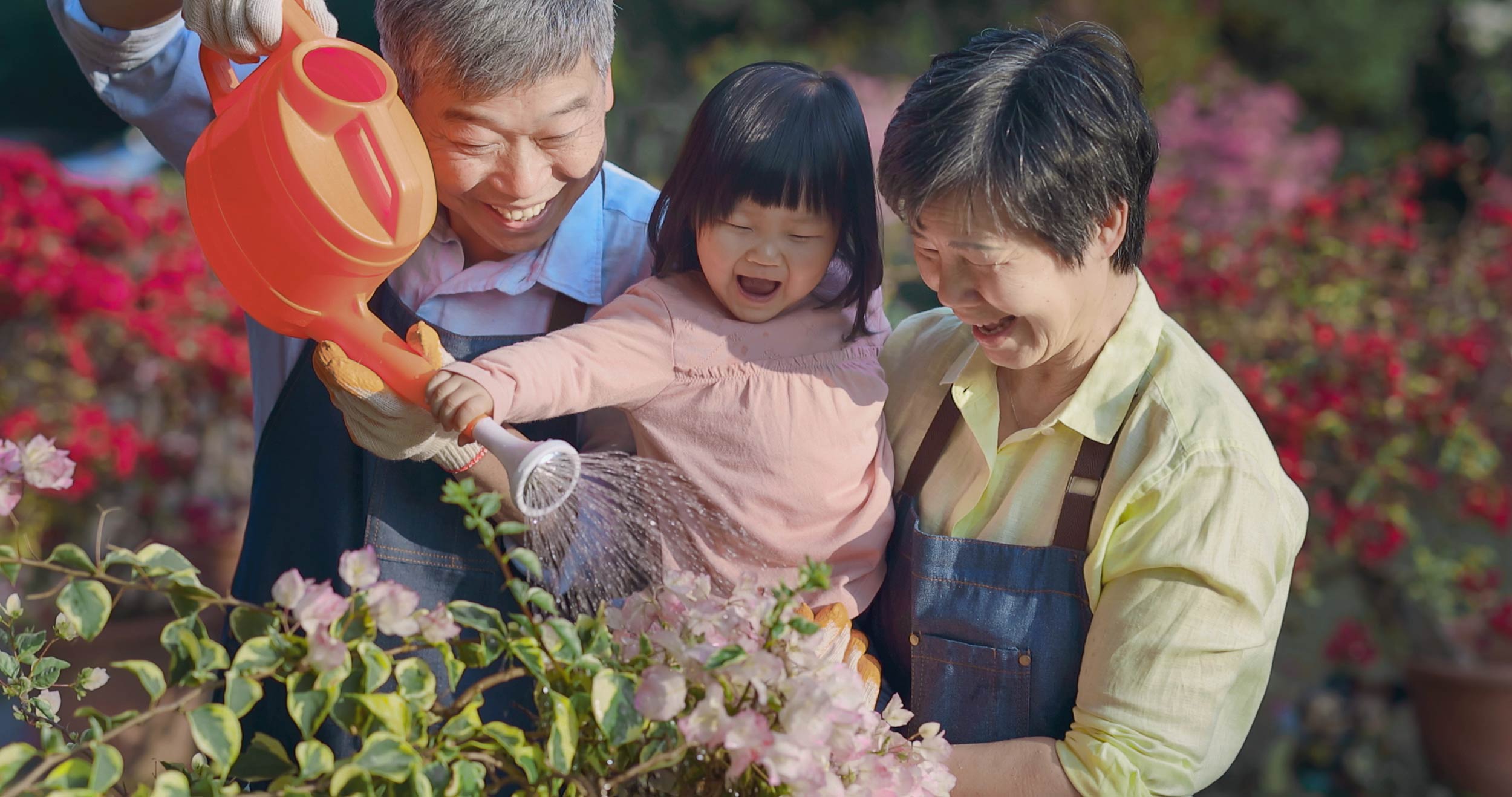 an older couple helping a young child water plants outdoors
