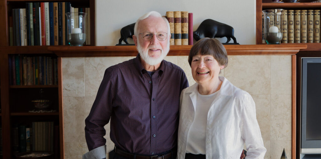 Older couple standing together and smiling in a living room.